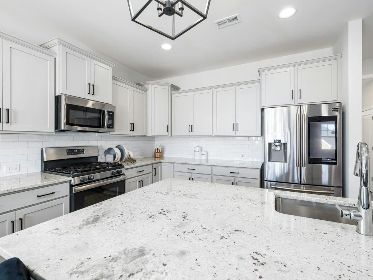 Light gray shaker kitchen with stainless appliances and a large island finished in speckled white-and-gray granite