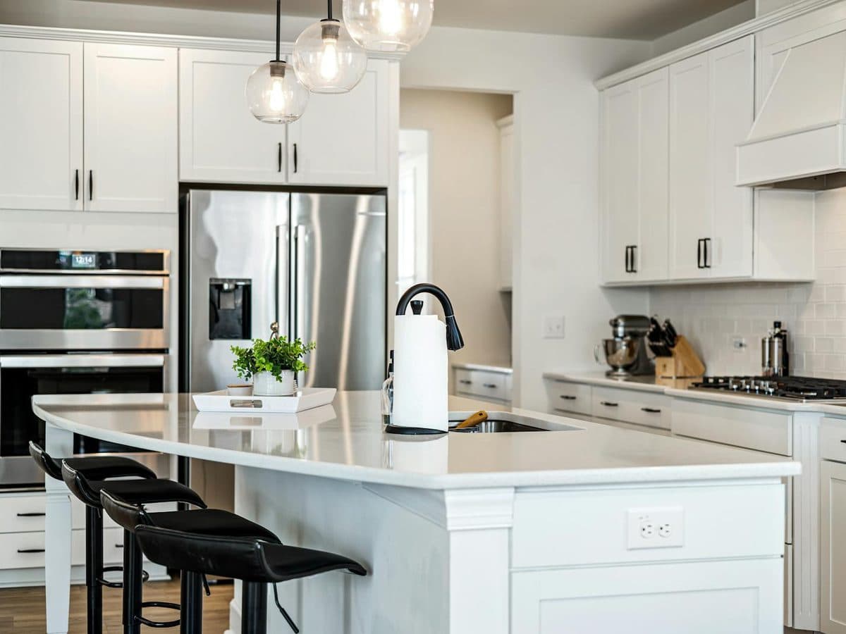 Bright white kitchen with shaker cabinets, glass pendant lights, and a large island topped with a clean white quartz countertop