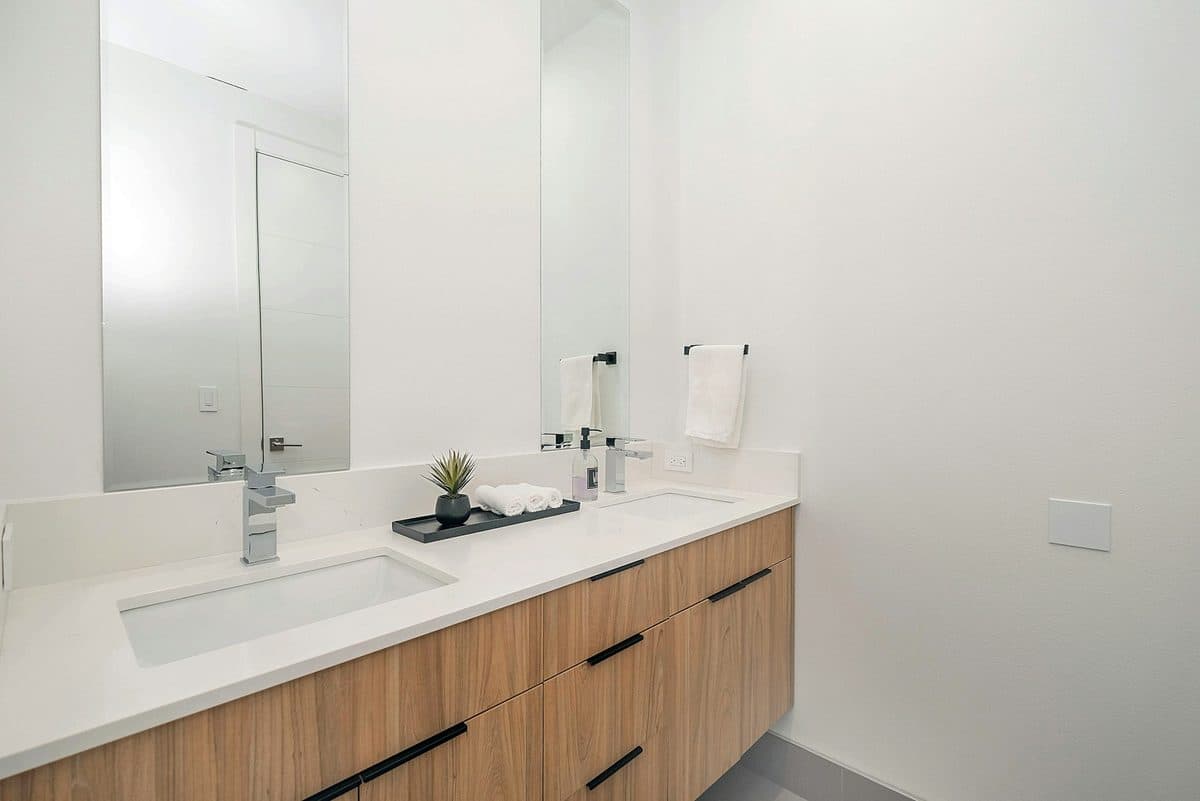 Modern bathroom vanity with a white quartz countertop, wood cabinetry, undermount sinks, and a frameless rectangular mirror