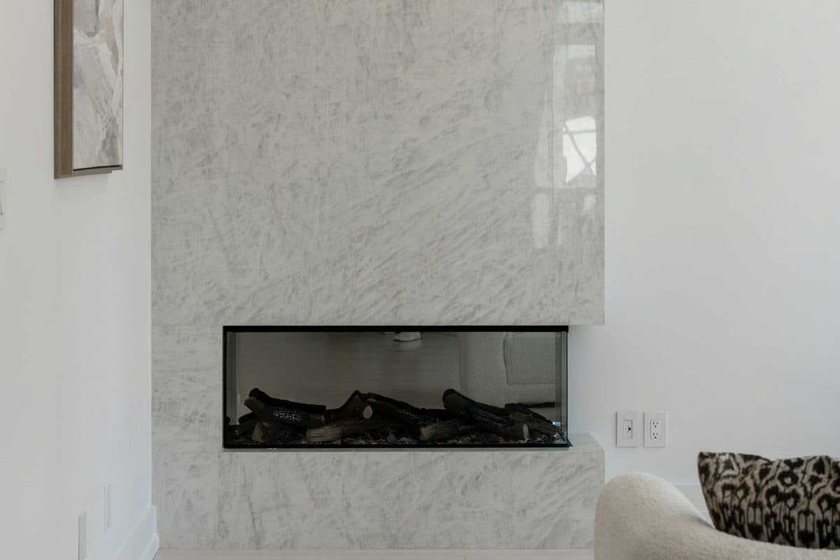 Modern floor-to-ceiling white marble slab fireplace surround with a linear gas firebox in a bright, minimalist living room