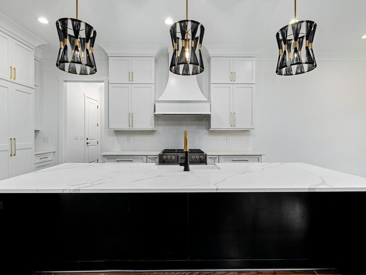 White kitchen with shaker cabinets, black-and-gold pendant lights, and an island topped with soft gray-veined white marble on a black base